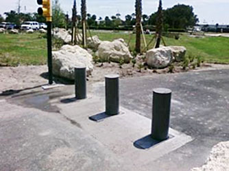 three retractable bollards at a stoplight with large rocks on the left side of the roadway