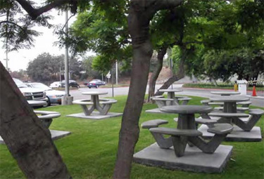 Small park next to an office parking lot in and gated entrance featuring all in one picnic tables.