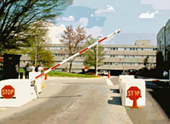 Vehicle entry gate with a crash beam in a semi-raised position and two concrete anchors on each side displaying stop signs