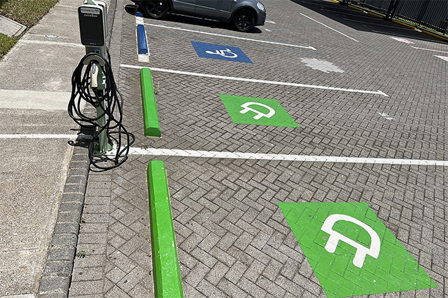 parking lot focused on two spaces with bright green concrete bumpers and green electric plug logos painted on the surface to designate the spaces as electric vehicle charging station partking, between the concrete bumpers is the electric charging station