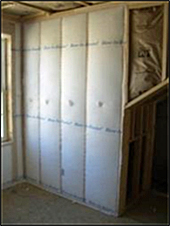 example of a wall being constructed with fiberglass insulation (white paper covering) between the joists