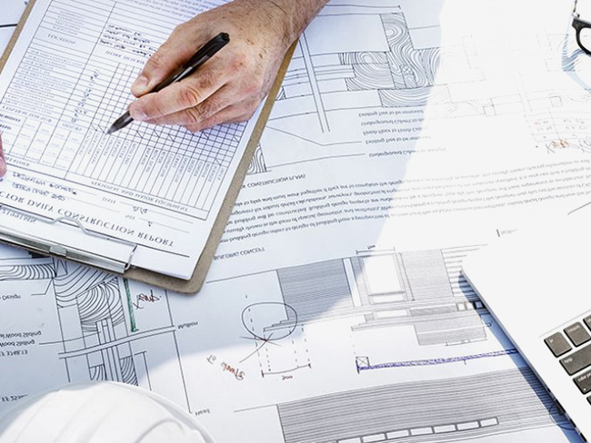 stock photo of a hand holding a pen over a clipboad with building plans spread out