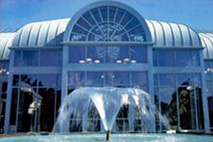 Entrance to a building with a fountain out front large windows and a curved metal roofing system
