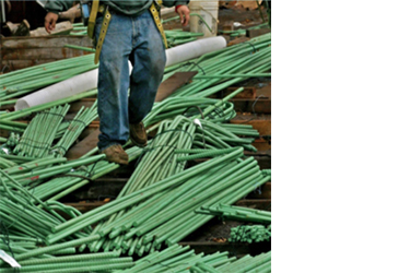 worker standing atop coated reinforcing steel haphazardly storaged with damaged surfaces and rust