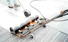 APP modified bitumen cap sheet being applied with a multi-head torch, the seam is being rolled with a roller