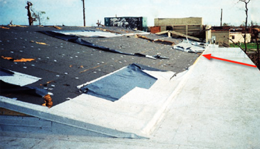 Photo of a building where a missile struck the fully adhered low-sloped roof and slid into the steep-sloped reinforced mechanically attached single-ply membrane