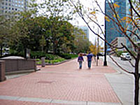 Two pedestrians walking along a wide path with a heavily raised planted berm on the left side to protect the courthouse beyond