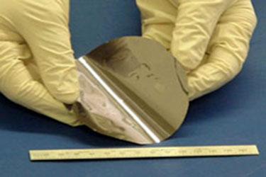Photo of two hands with latex gloves holding a circular solar cell structure against a ruler to show that it is under a foot in diameter