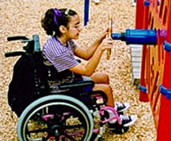 Photo of a child seated in wheelchair on a playground playing with an activity board