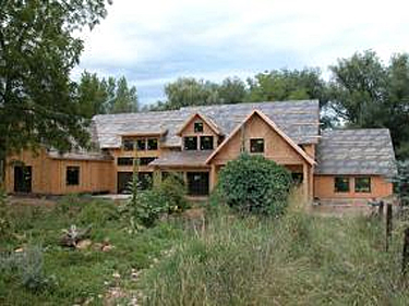 Full front view including trees and bushes of house construction using SIPs for wall and roof panels in a complicated architectural form