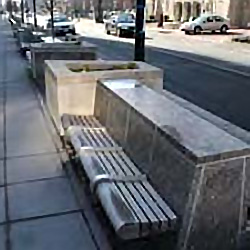 hardened site furniture-a bench for seating facing away from the street built on the backside of a planter along the curb