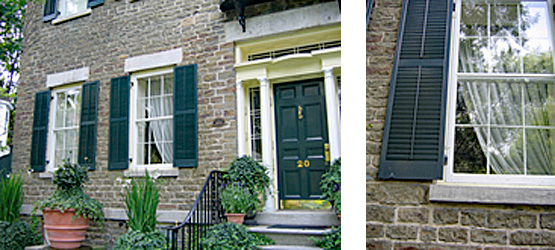 2 photos: on left is the view of the front of a 19th century brick house showing the black front door and two windows off to the left side with potted plants in the front; on the right a close up view of a black shutter and window on a 19th century brick house. The historic storm windows protect the original windows.